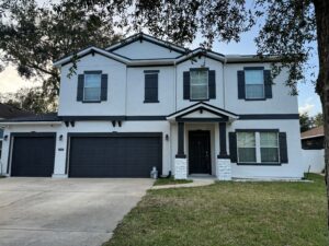 Modern two-story house with white stucco exterior, black shutters, and a black front door, with a three-car garage and a small front lawn.