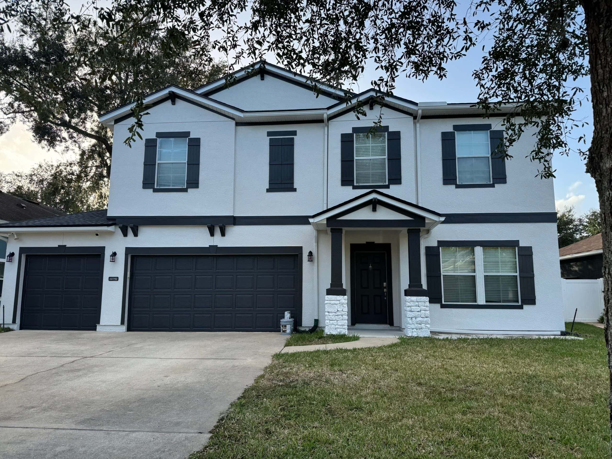 Modern two-story house with white stucco exterior, black shutters, and a black front door, with a three-car garage and a small front lawn.