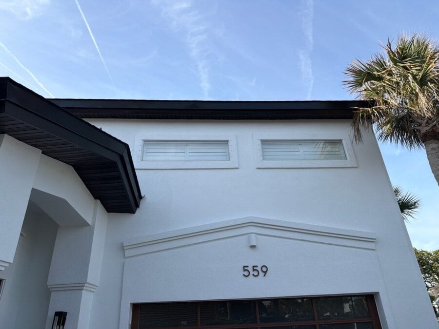 White modern house with the number 559, black roof, and palm trees against a blue sky.