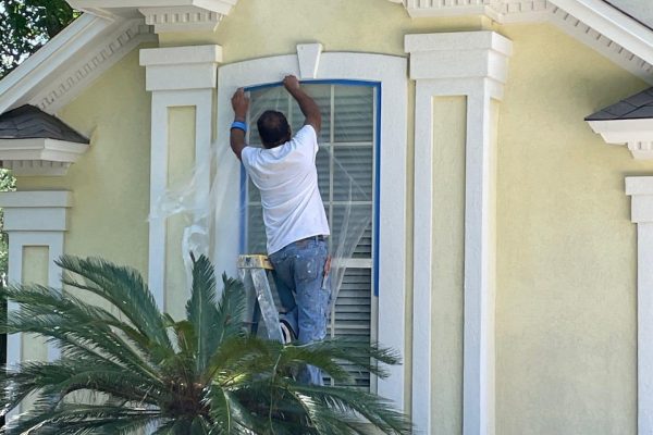 worker taping window cover during painting process
