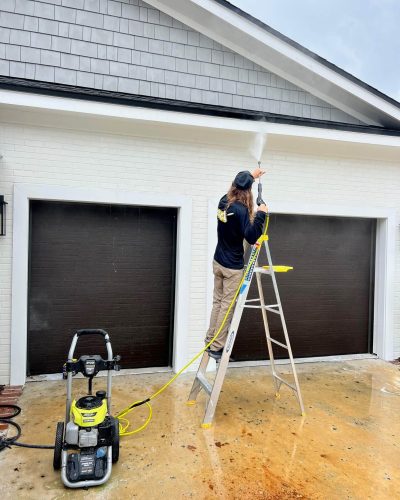 man on ladder pressure washing garage