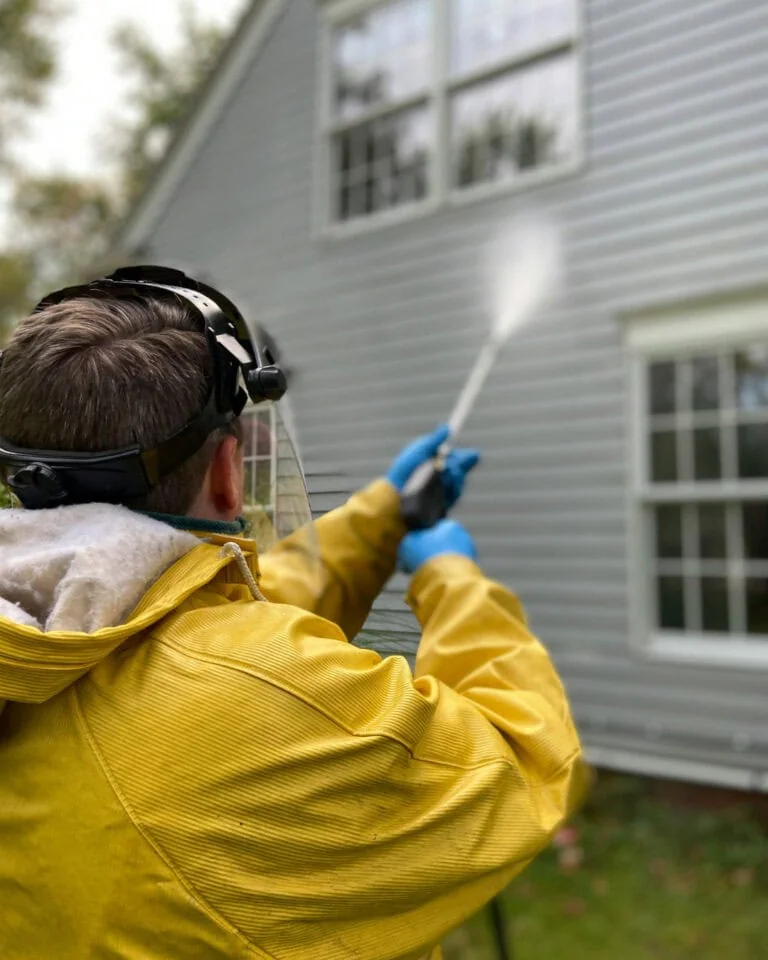 man pressure washing siding of a house